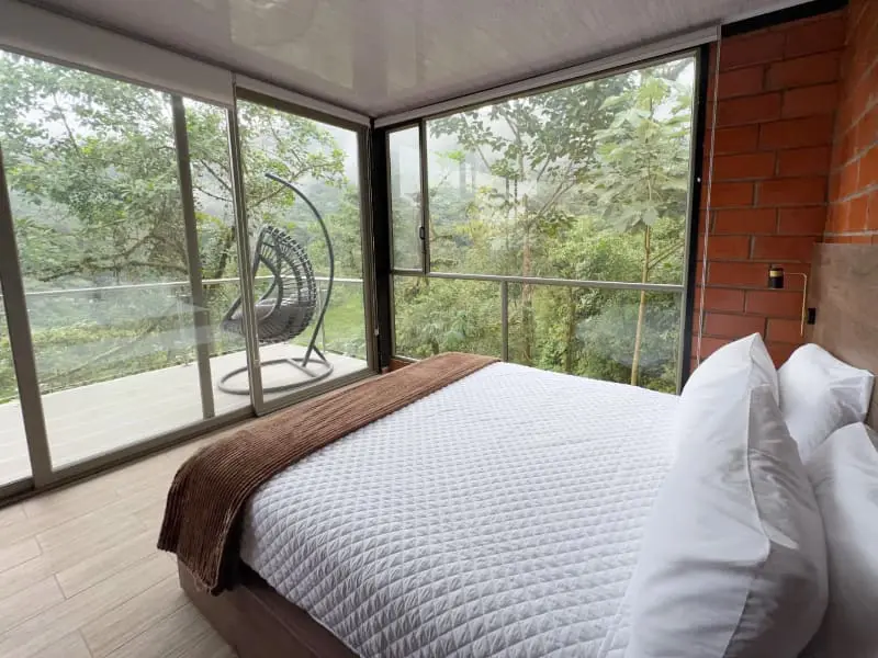 Master bedroom in the Mashpi Amagusa Guest House with glass walls and cloud forest views.